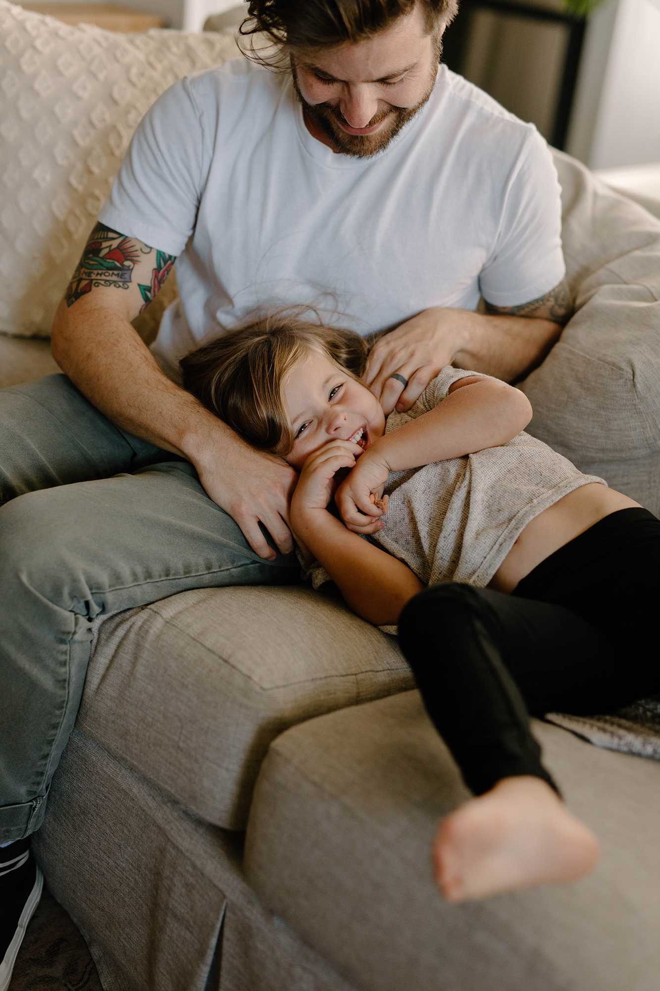 A father and child laugh while relaxing on a couch