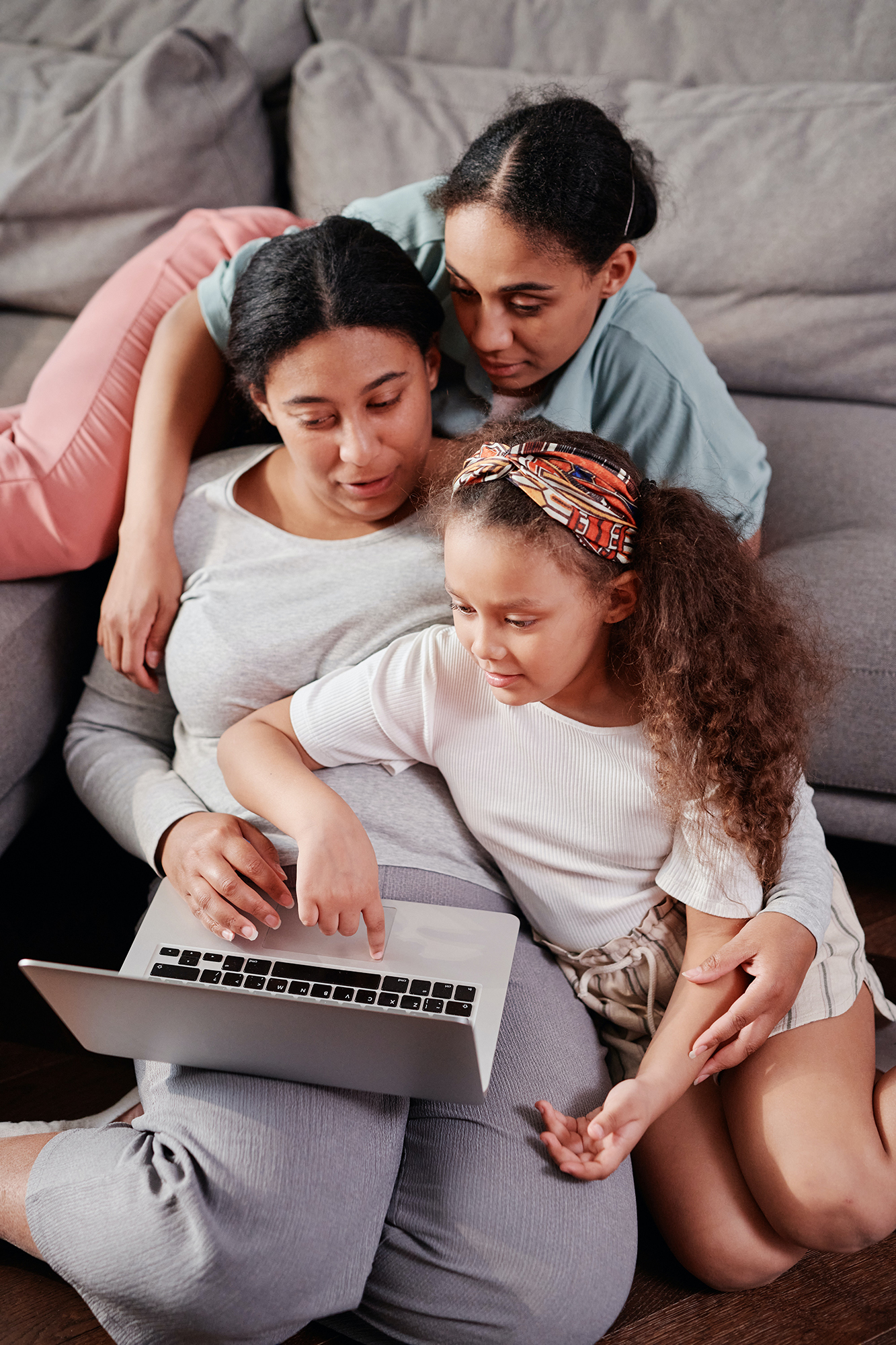 A mother and her daughters on a couch look at a laptop together